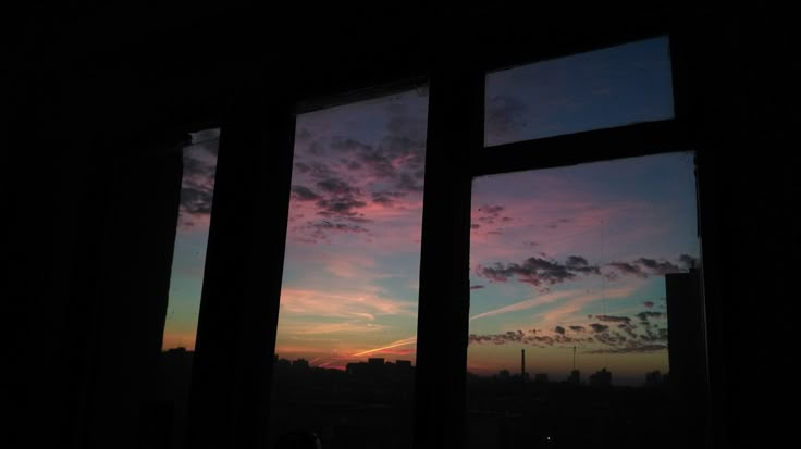 the sun is setting over some buildings and clouds in the sky as seen from a window