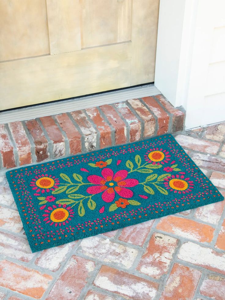 a blue door mat with flowers on it sitting in front of a brick wall next to a white door