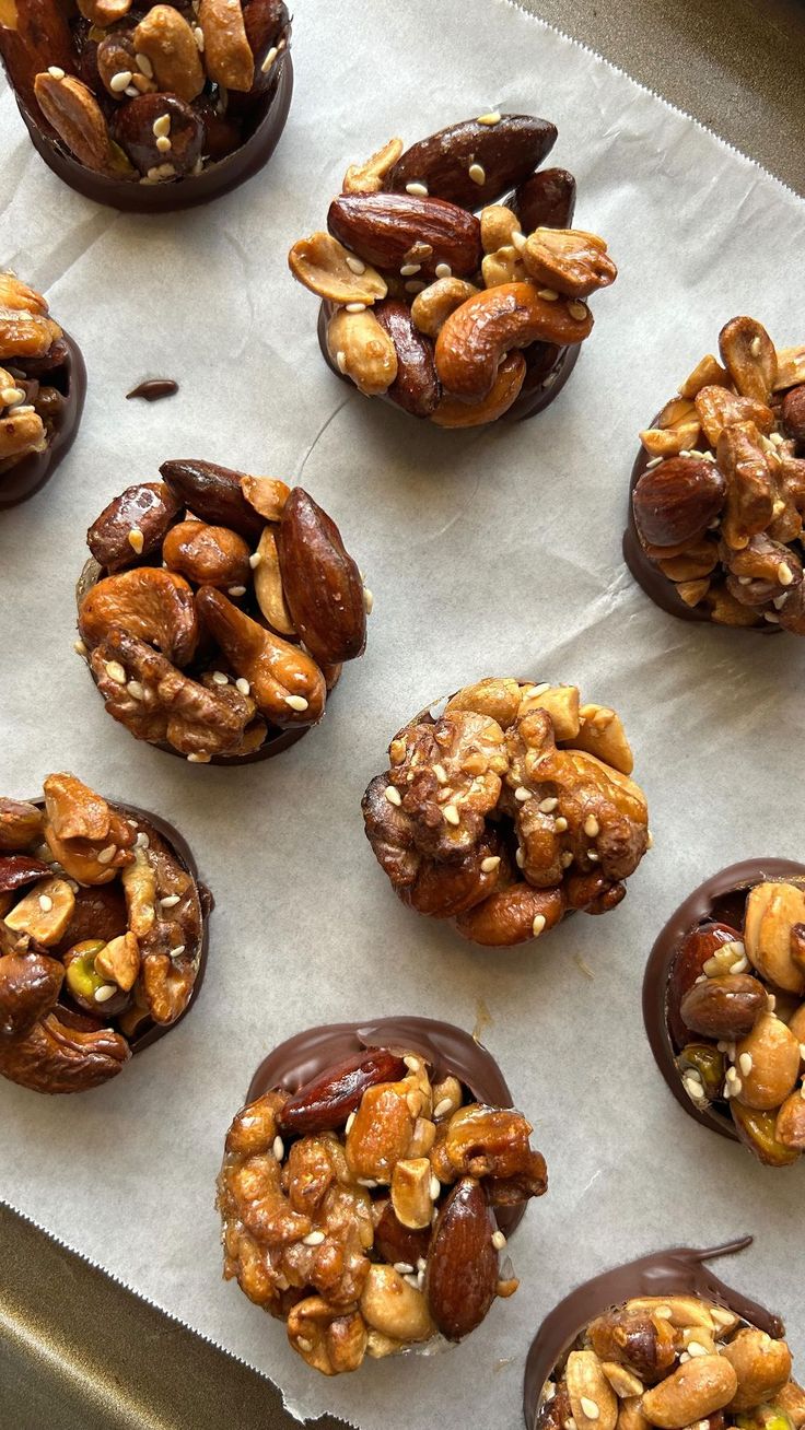 chocolate covered donuts with nuts and walnuts on top, lined up on parchment paper