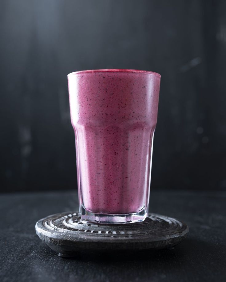 a glass filled with pink smoothie sitting on top of a black table next to a plate