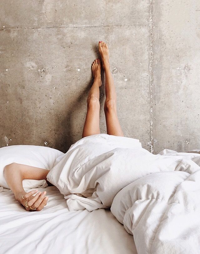 a woman laying in bed with her feet up on the pillow and sheets pulled back