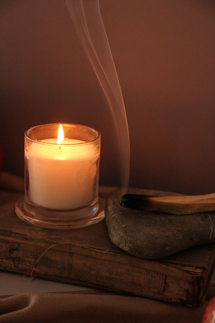 a lit candle sitting on top of a wooden table next to an apple and rock