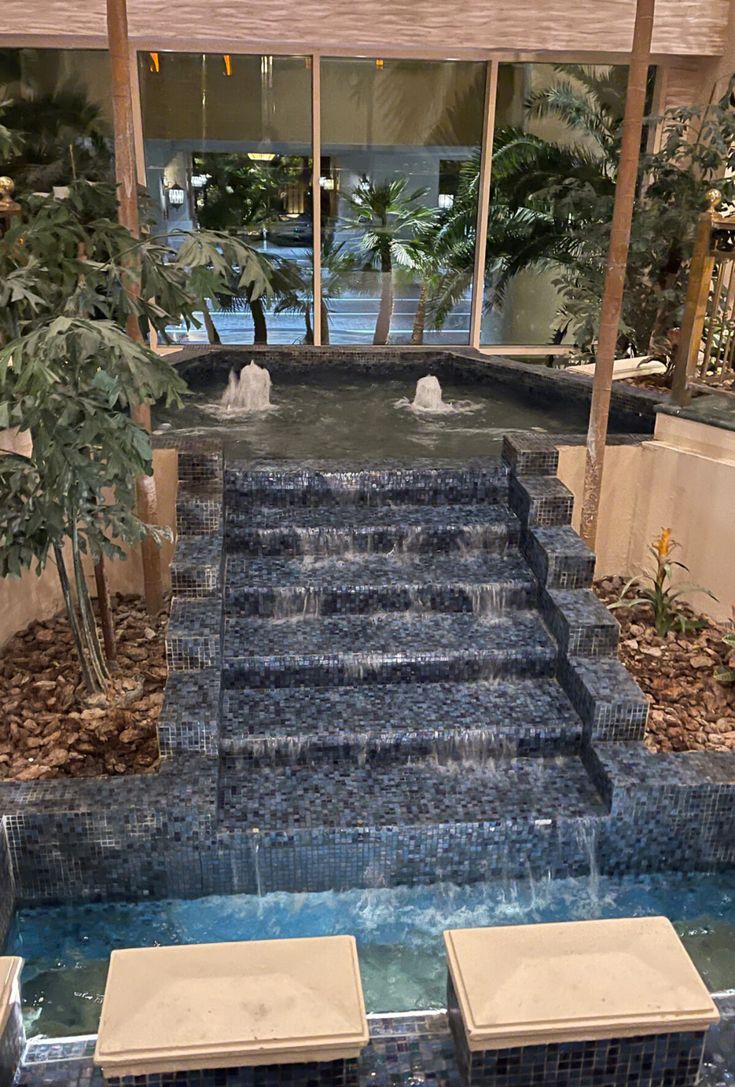 an indoor swimming pool with steps leading up to the water feature and trees in the background