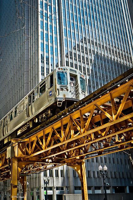 a train traveling over a bridge in front of tall buildings with skyscrapers behind it