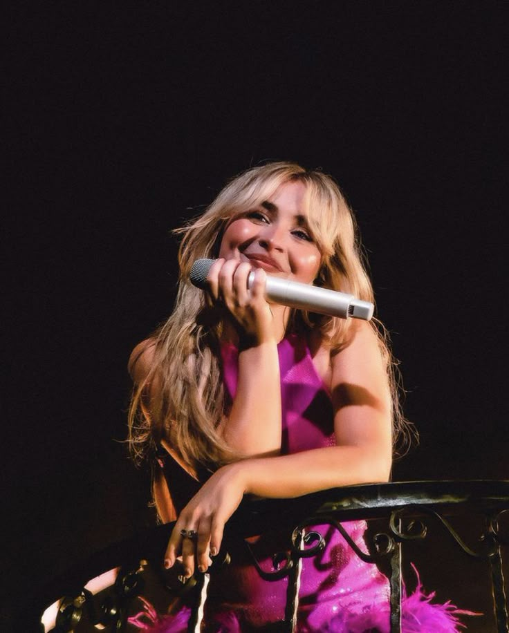 a woman in a pink dress holding a microphone and singing into the microphone with her hand