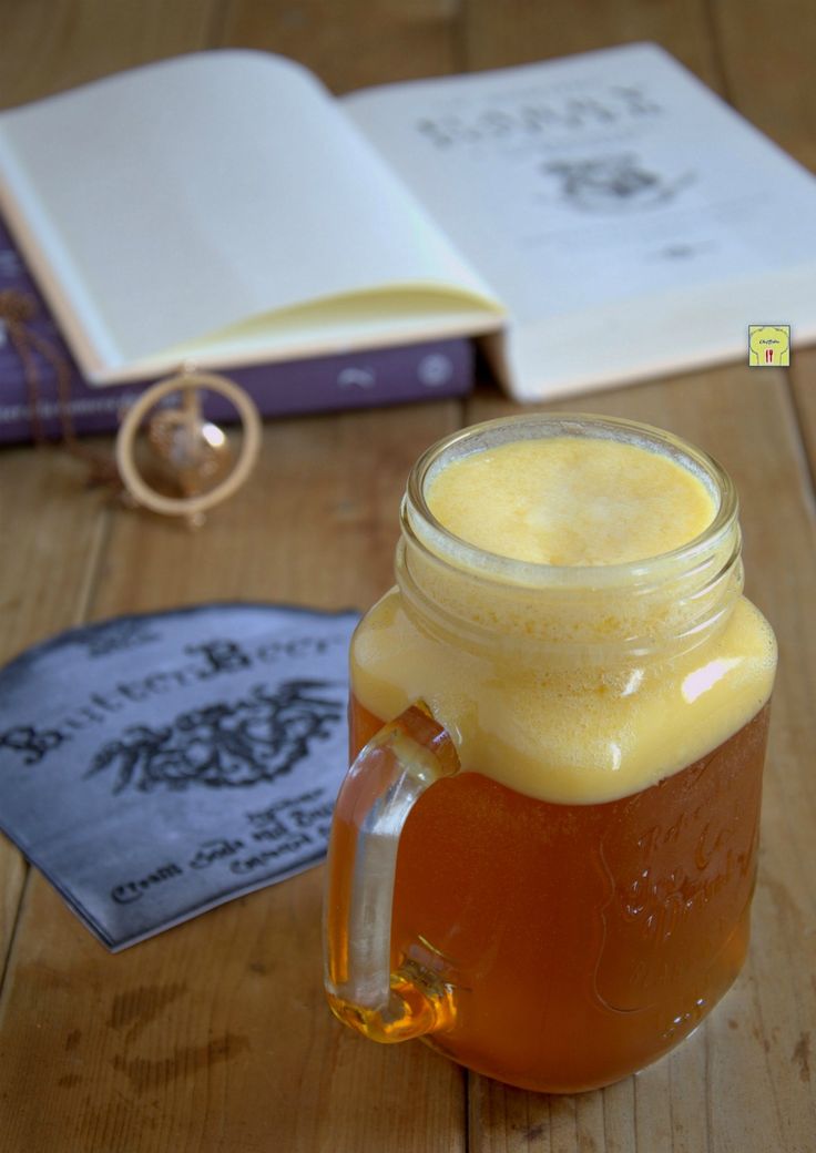 a glass mug filled with liquid sitting on top of a wooden table next to an open book