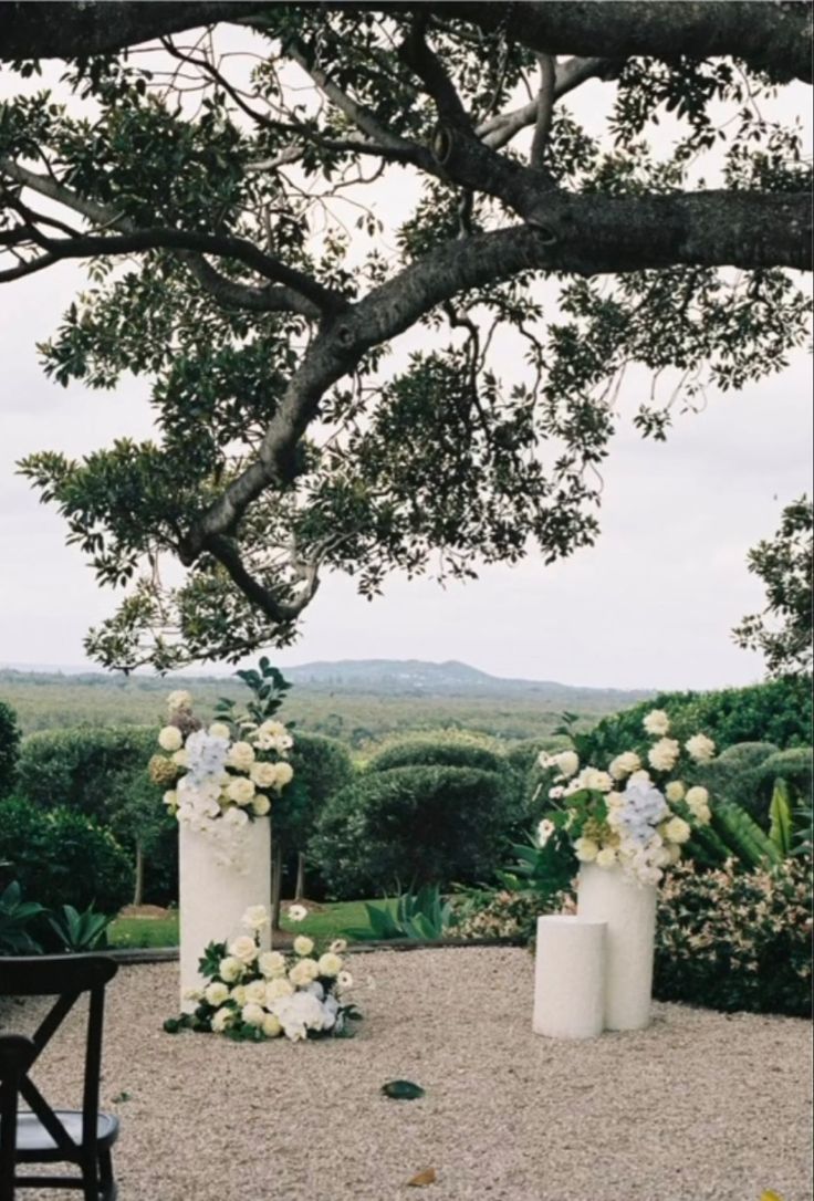 an outdoor ceremony set up with white flowers and greenery on the ground under a large tree