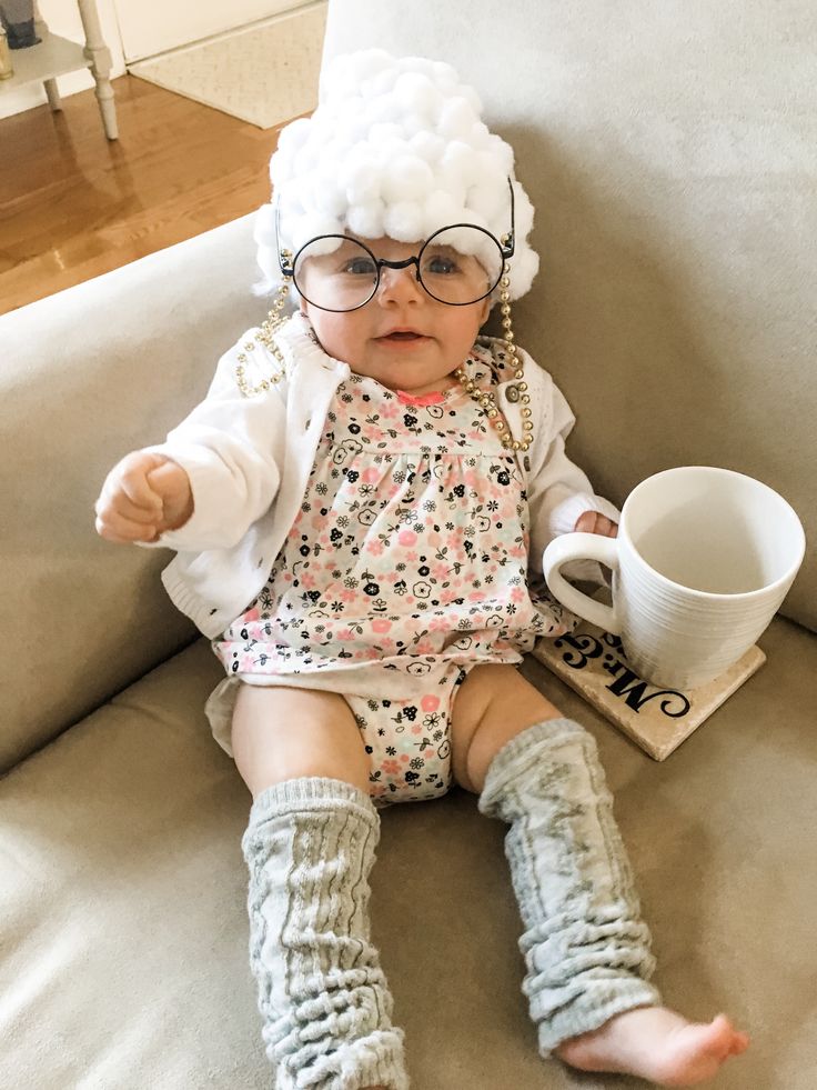 a baby sitting on a couch holding a coffee cup and wearing glasses with her legs crossed