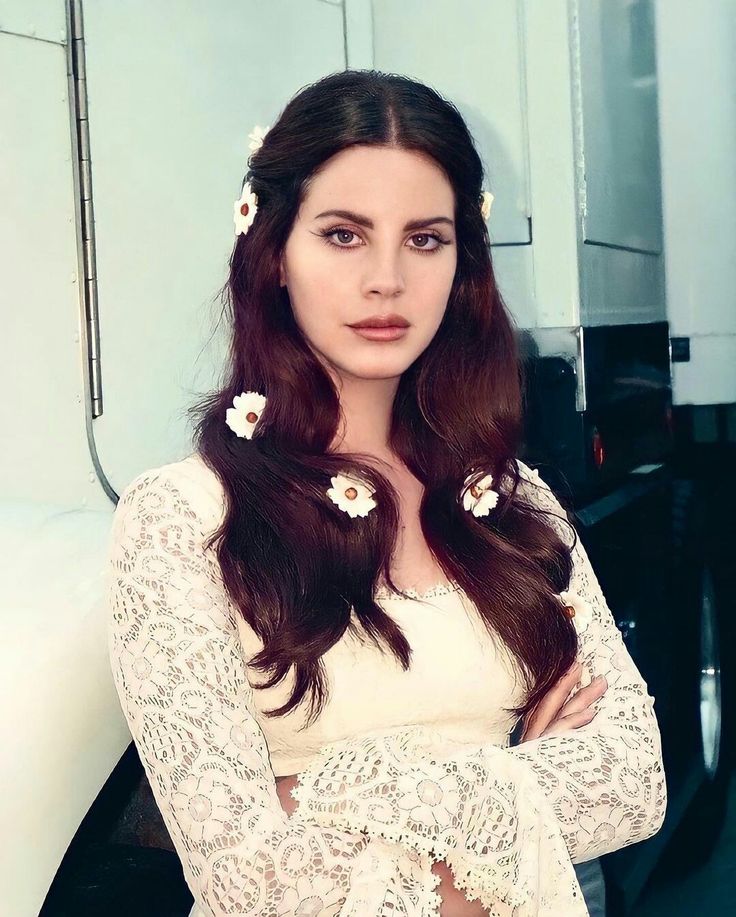 a woman standing with her arms crossed and flowers in her hair, wearing a white top