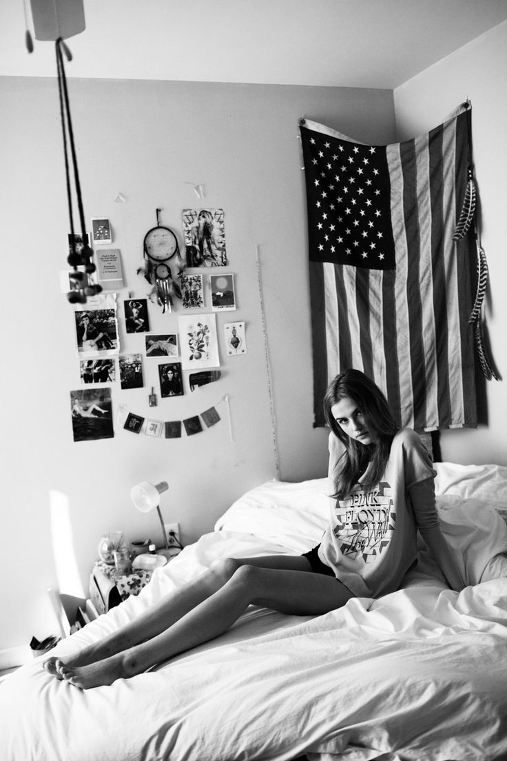 a woman sitting on top of a bed in front of an american flag hanging above her head