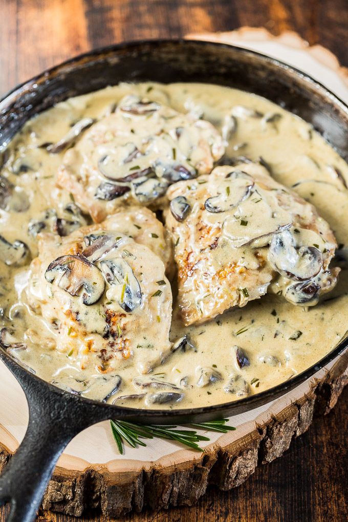 a skillet filled with chicken and mushroom gravy on top of a wooden table