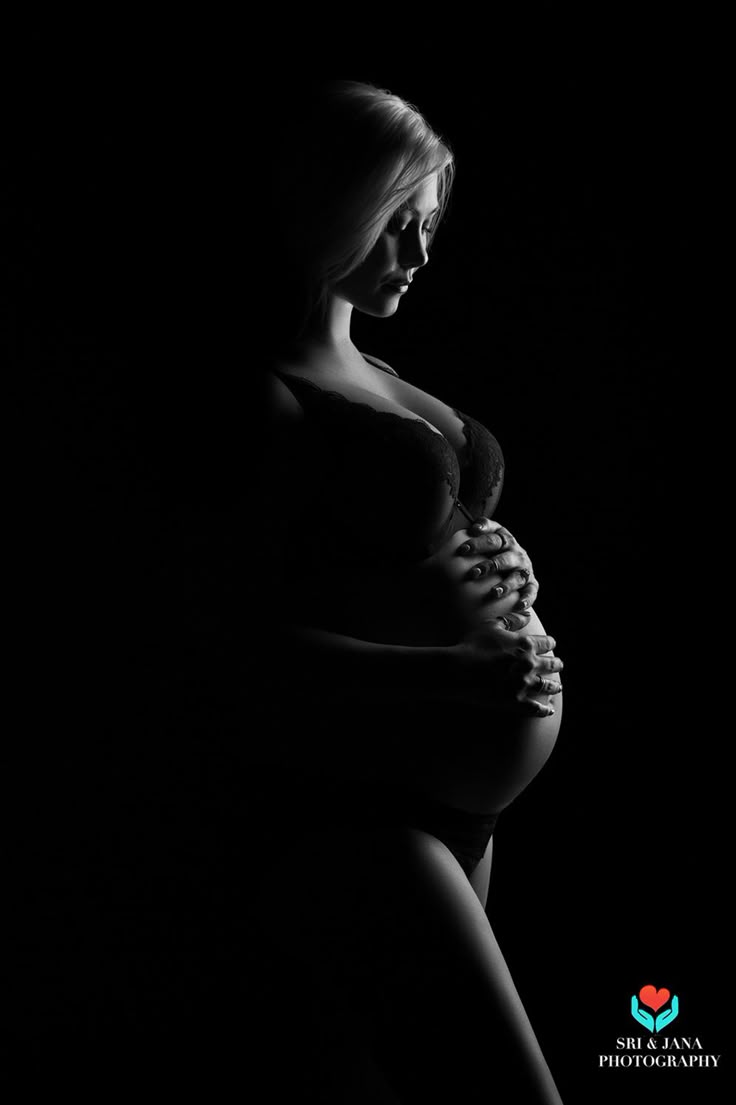 a pregnant woman standing in the dark with her hands on her stomach