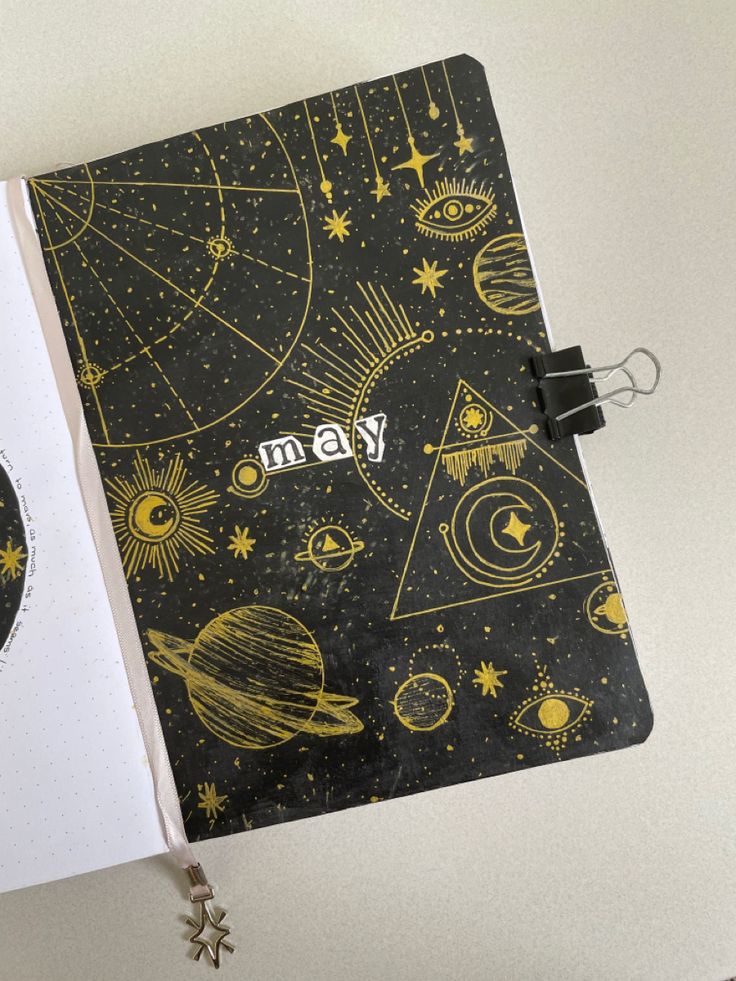 an open notebook with the word may written in gold on it and space themed background