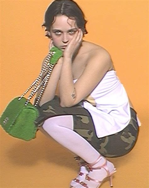 a woman kneeling down with a green purse on her hand and holding a cell phone to her ear