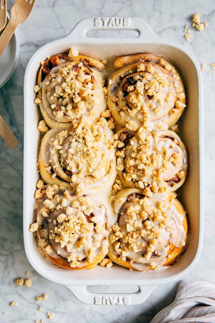 a baking dish filled with cinnamon rolls covered in icing and crumbled toppings