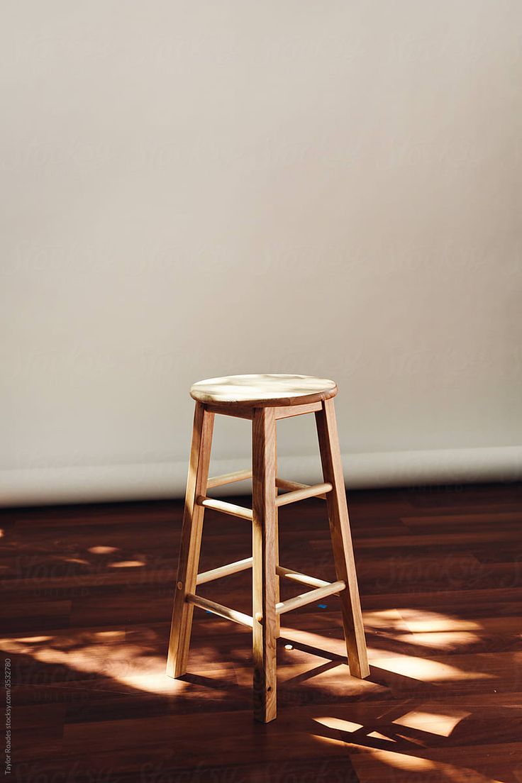 a wooden stool sitting on top of a hard wood floor next to a white wall