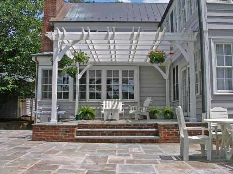 an outdoor patio with white chairs and a pergolated area in front of the house