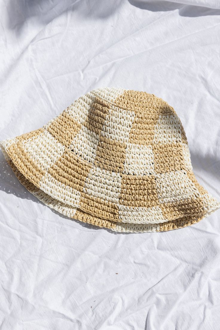 a crocheted hat laying on top of a white bed sheet with the sun shining