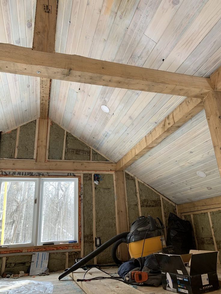 an unfinished room with wood paneling and exposed ceiling, including a laptop on the floor