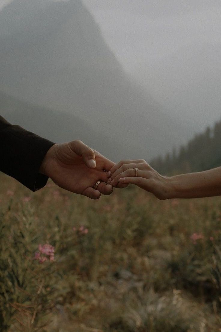 two people holding hands in front of mountains