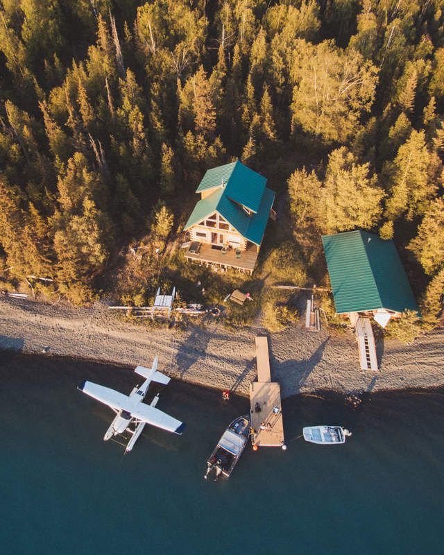 an aerial view of two small planes parked in front of a cabin on the water