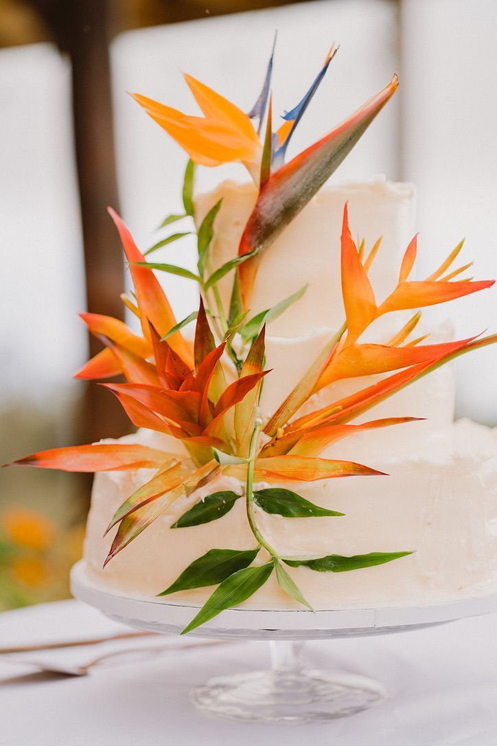 a wedding cake with orange and green flowers on the frosting is sitting on a table