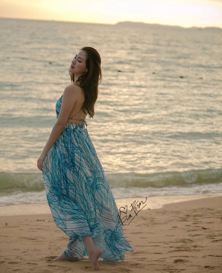 a woman standing on top of a sandy beach next to the ocean with her eyes closed