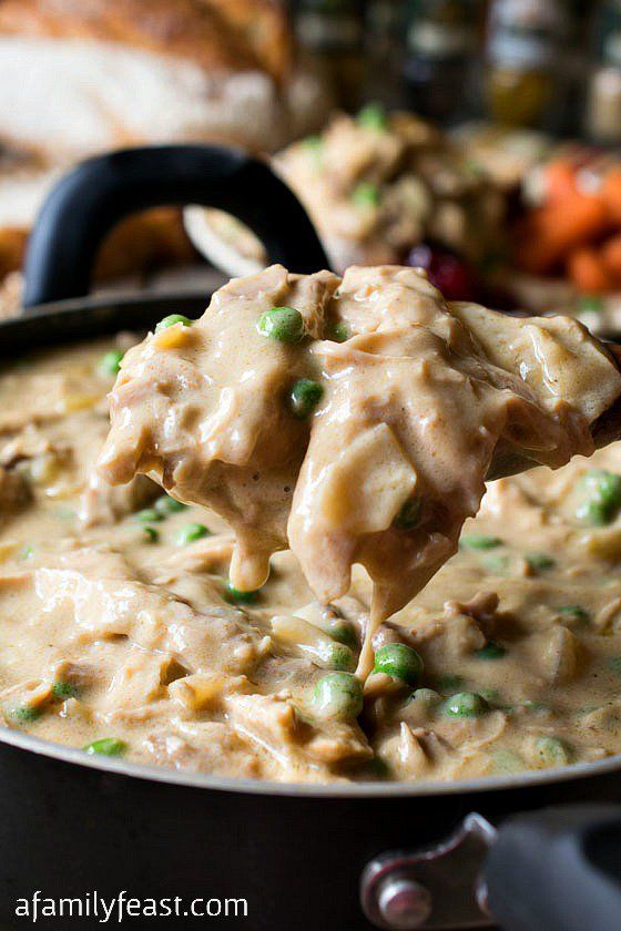 a ladle full of chicken and peas in a cream sauce with carrots on the side