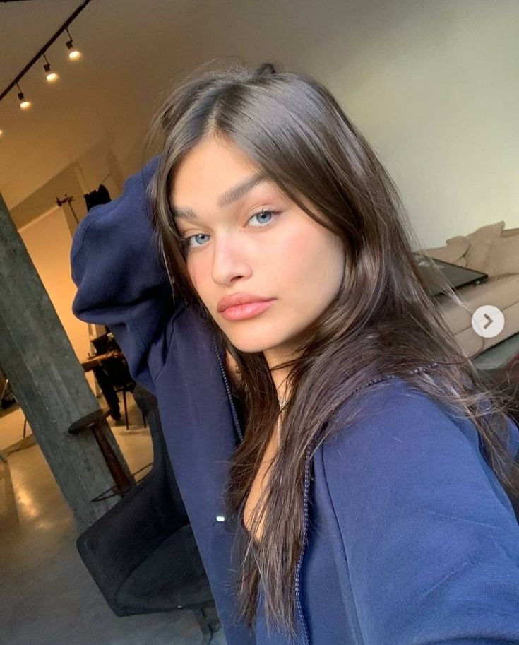 a woman with long hair and blue shirt posing for a photo in a living room