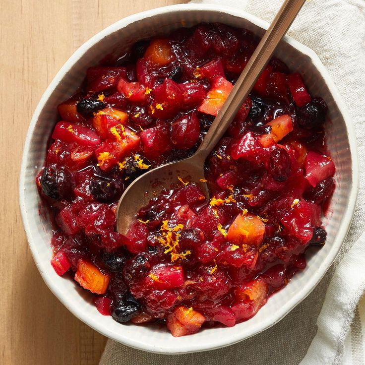 a white bowl filled with cranberry sauce on top of a wooden table next to a spoon