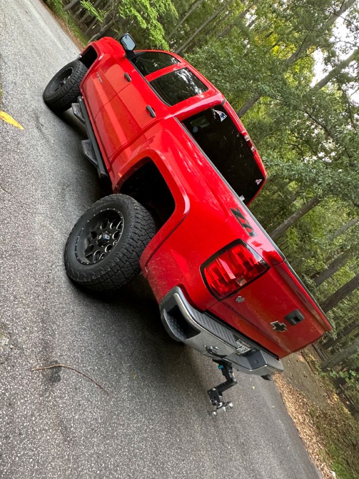 a red pick up truck that is upside down on the side of the road in front of some trees