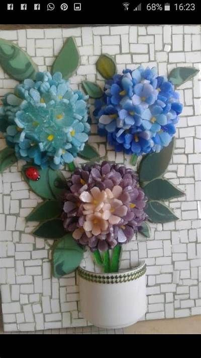 three paper flowers in a white vase on a mosaic tile wall behind them is a lady bug