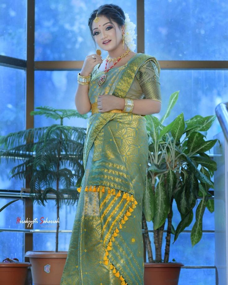 a woman in a green and yellow sari standing next to a potted plant