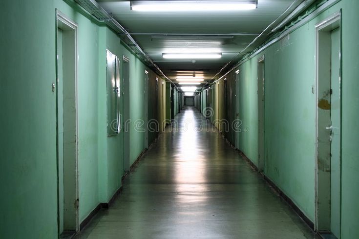 an empty long hallway with green walls and lights on the ceiling is lit by recess lighting