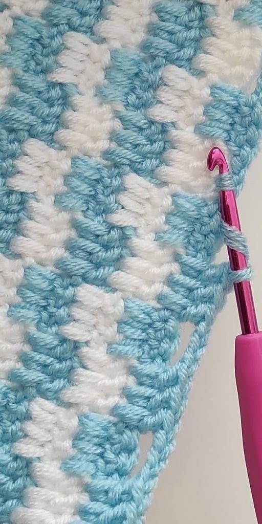 a crocheted blue and white blanket with a pink toothbrush sticking out of it