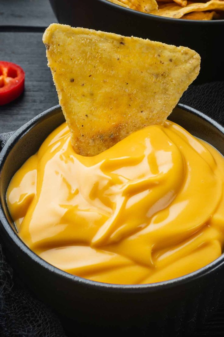 a tortilla chip being dipped with cheese sauce in a bowl next to some chips