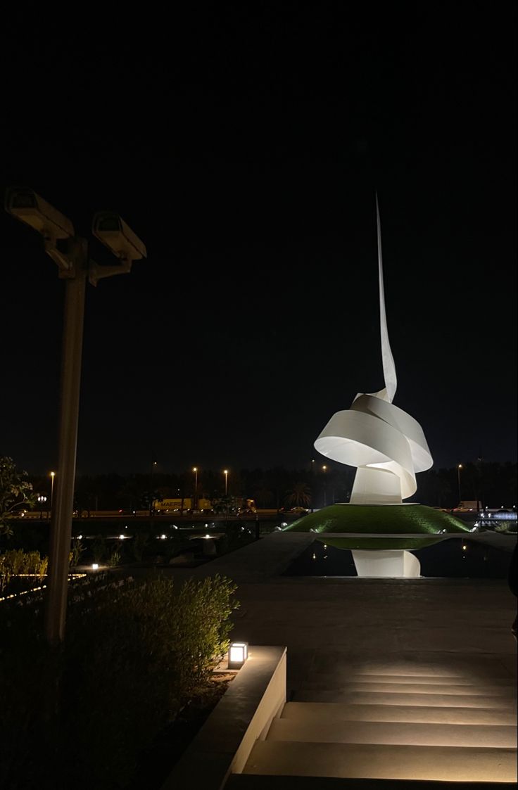 a large white sculpture sitting on top of a lush green field at night with buildings in the background