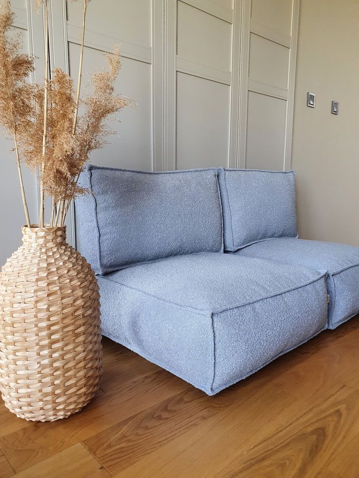 a blue couch sitting on top of a wooden floor next to a vase with dry grass in it