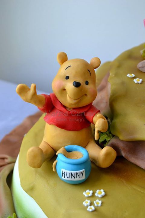 a winnie the pooh cake with fondant decorations on top and flowers around it