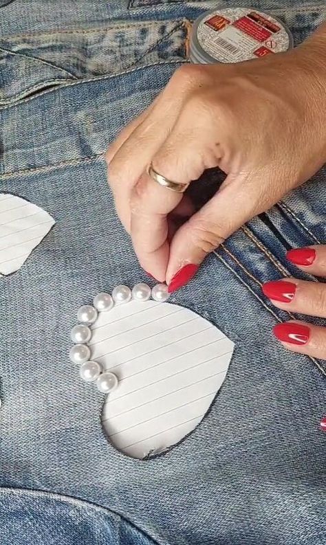 a woman with red nails is cutting out hearts on her jean pants, which are decorated with pearls and beads