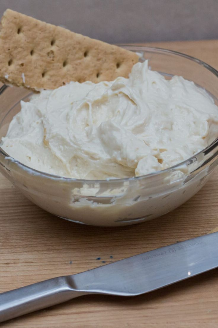 a glass bowl filled with whipped cream next to a cracker on a cutting board