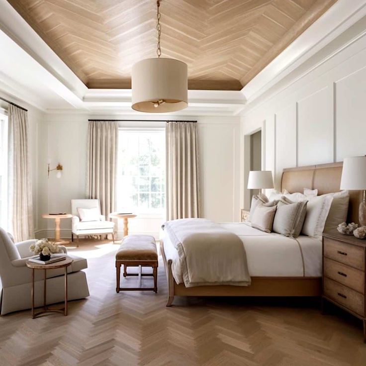 a bedroom with white walls and wood flooring has a large bed, two chairs, and a window