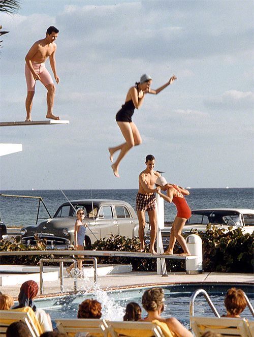 people are jumping into the pool and swimming in the water while others watch from chairs