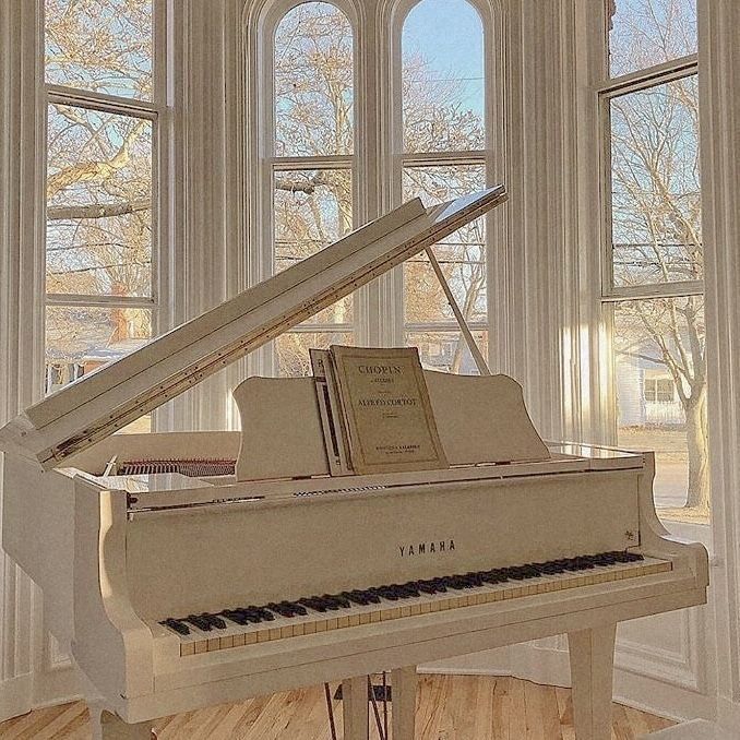 a grand piano sitting in front of a window next to a wooden floor and white walls