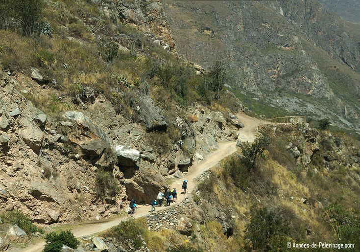 some people are walking on a path in the mountain side area with rocks and grass