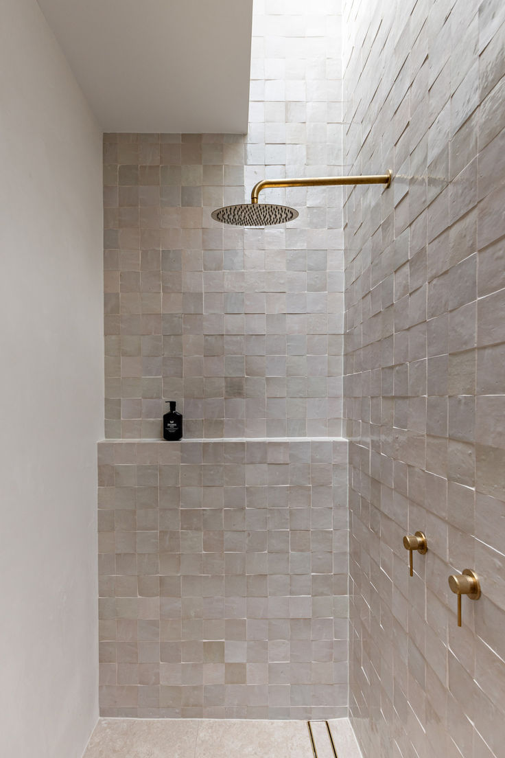 the shower head is mounted to the side of the wall in this tiled bathroom with gold fixtures