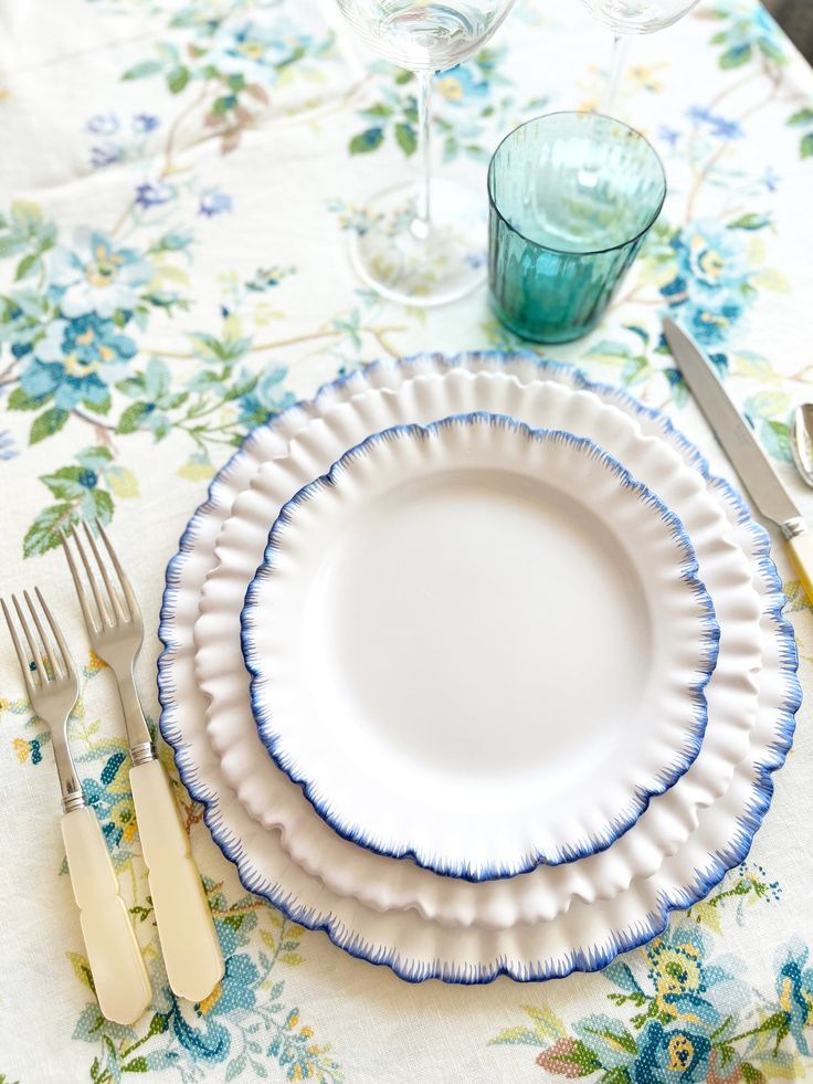 an empty plate with blue trim sits on a floral table cloth next to silverware