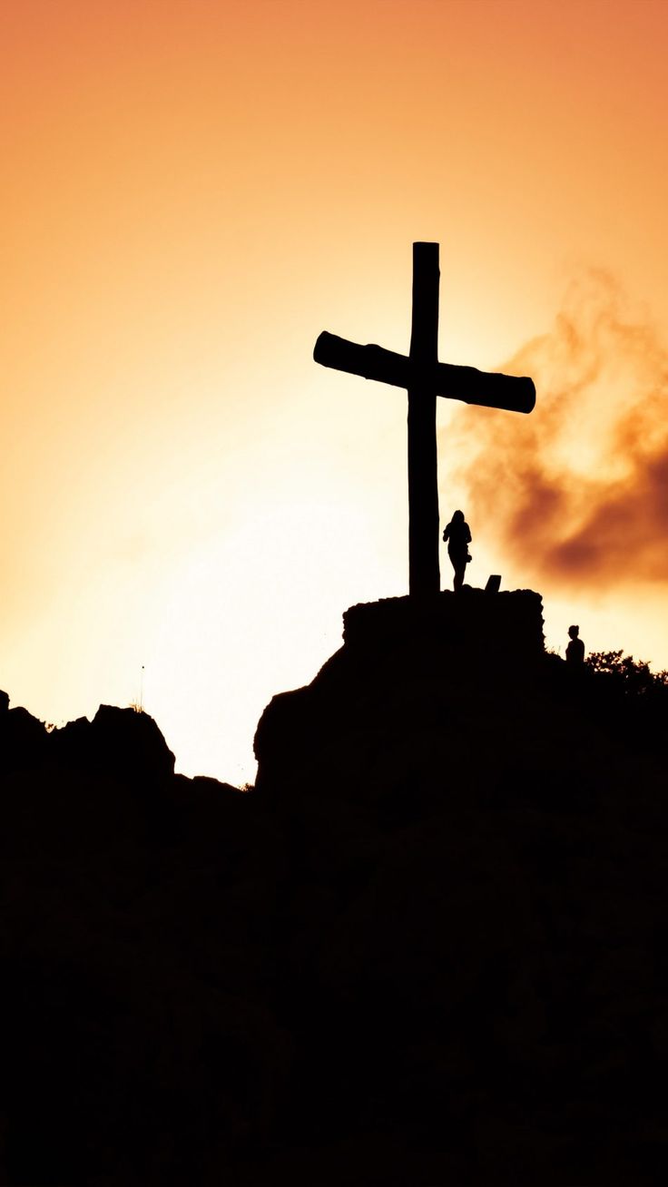 a cross on top of a hill with the sun setting behind it and clouds in the sky