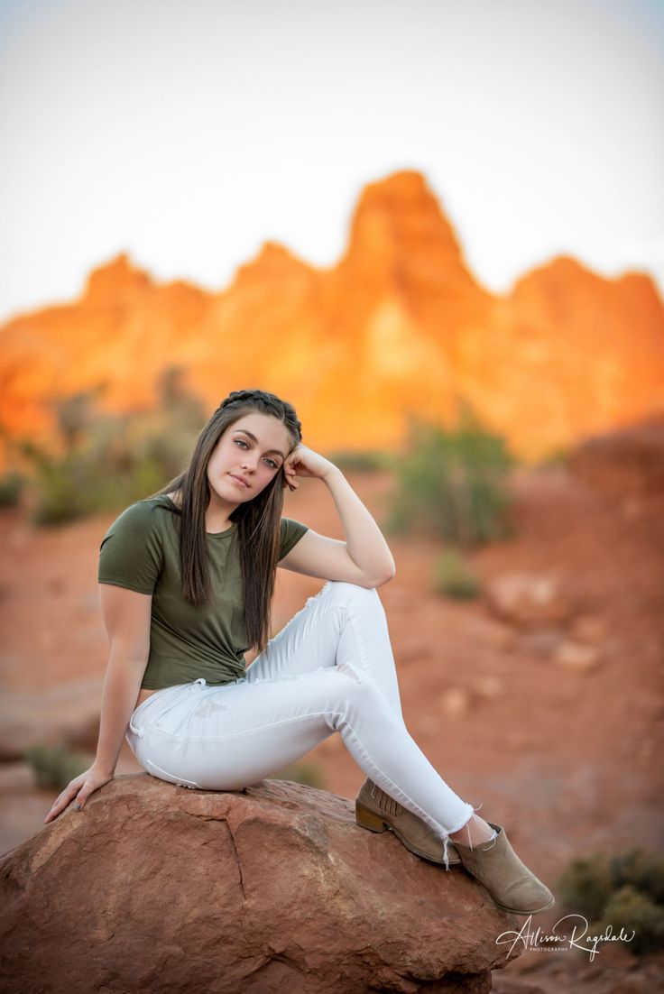 a young woman sitting on top of a rock in front of some rocks and mountains