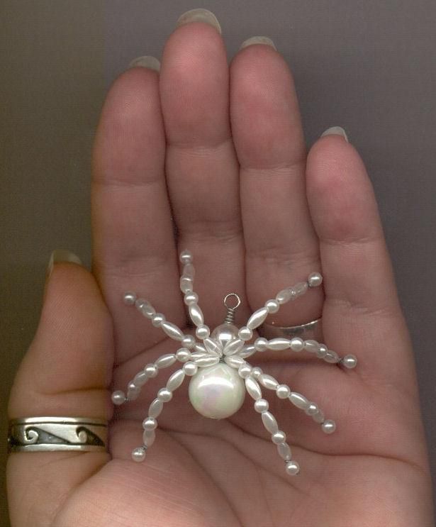 a hand holding a small white spider brooch with pearls on it's back